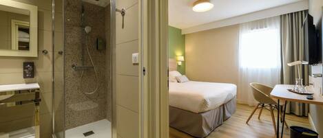 A hotel room with a shower, a bed, a desk, and a television.