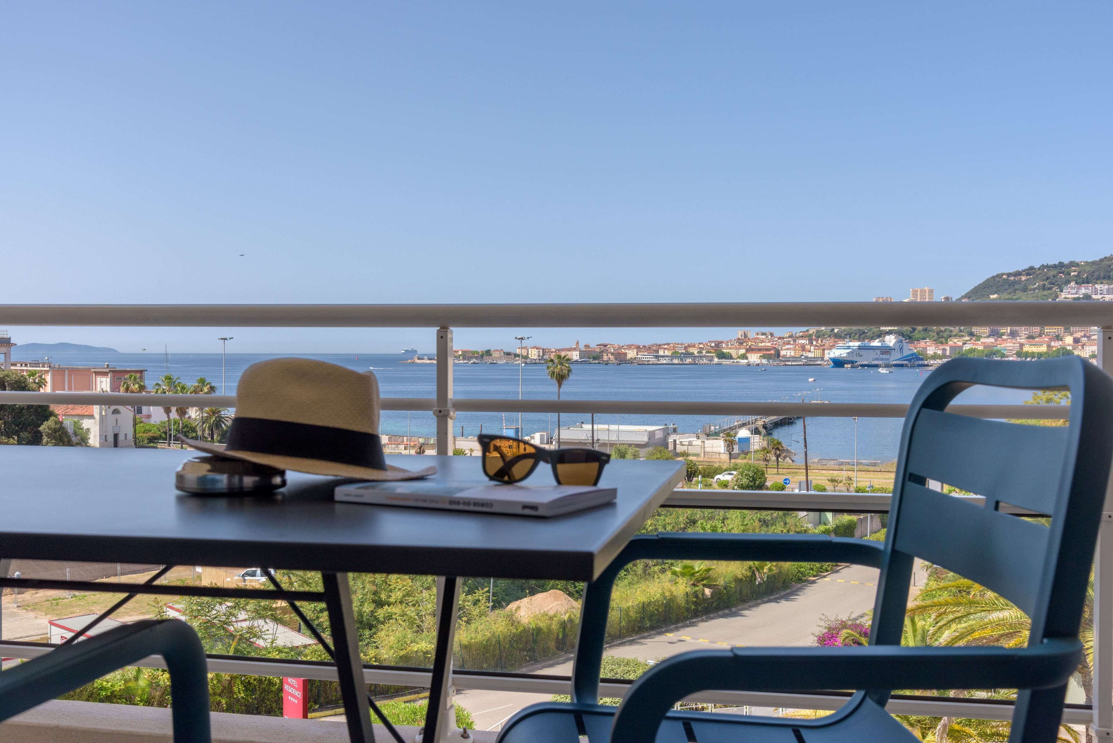 A balcony with a table, a chair, and a view of the sea and cityscape.