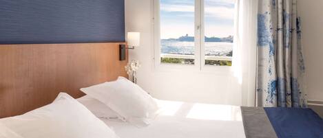 A hotel room with a large bed, a view of the water, and a window with curtains.
