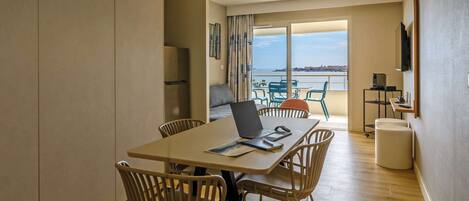 Un comedor moderno con una computadora portátil sobre la mesa, rodeado de sillas, y vistas al mar a través de amplias ventanas.
