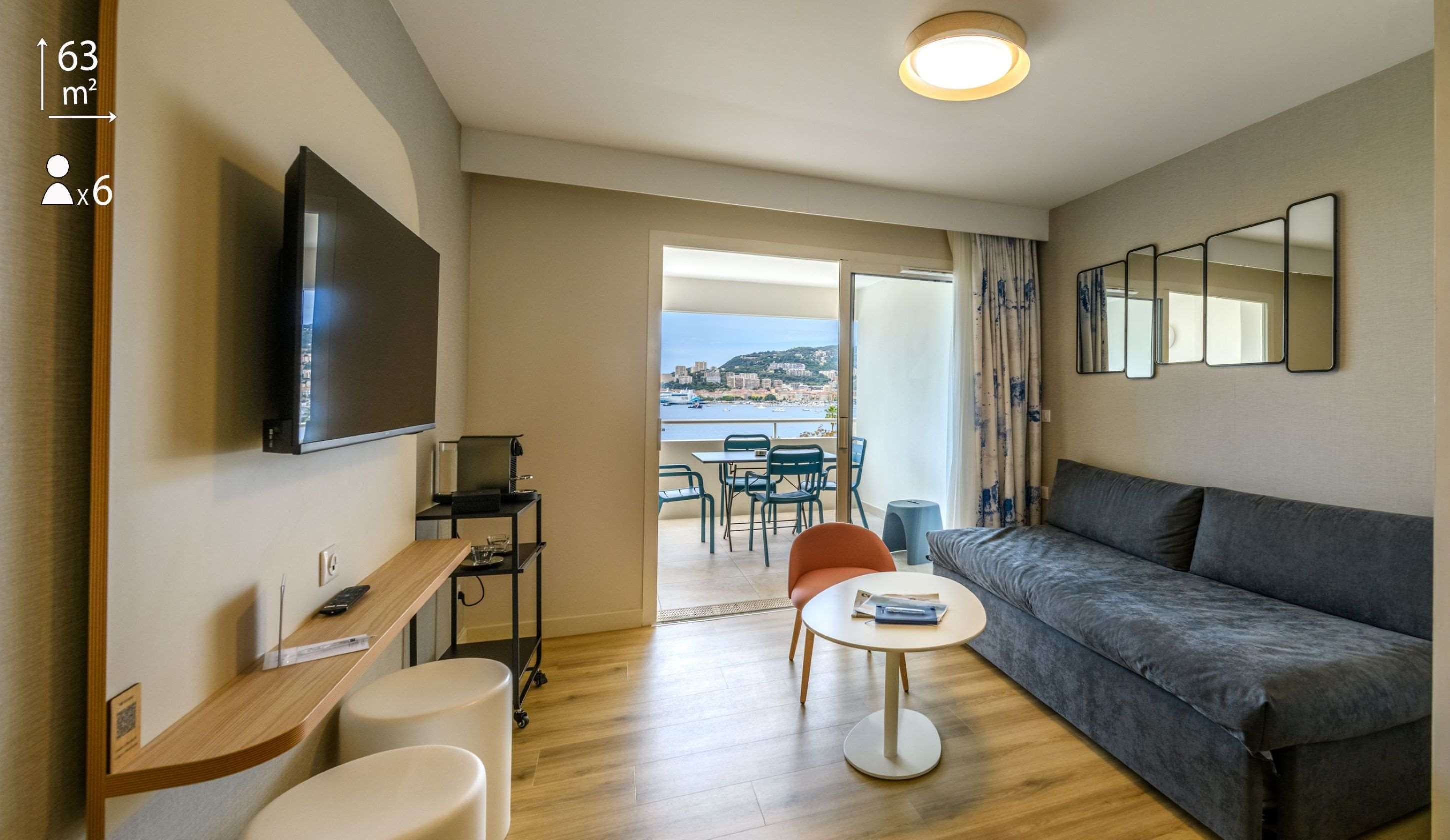 Una sala moderna con un sofá, un televisor, una mesita y un balcón con vistas al mar.