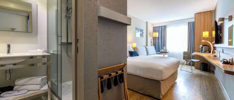 A modern hotel room with a shower, a bed, a desk, and a bathroom with a sink and mirror.