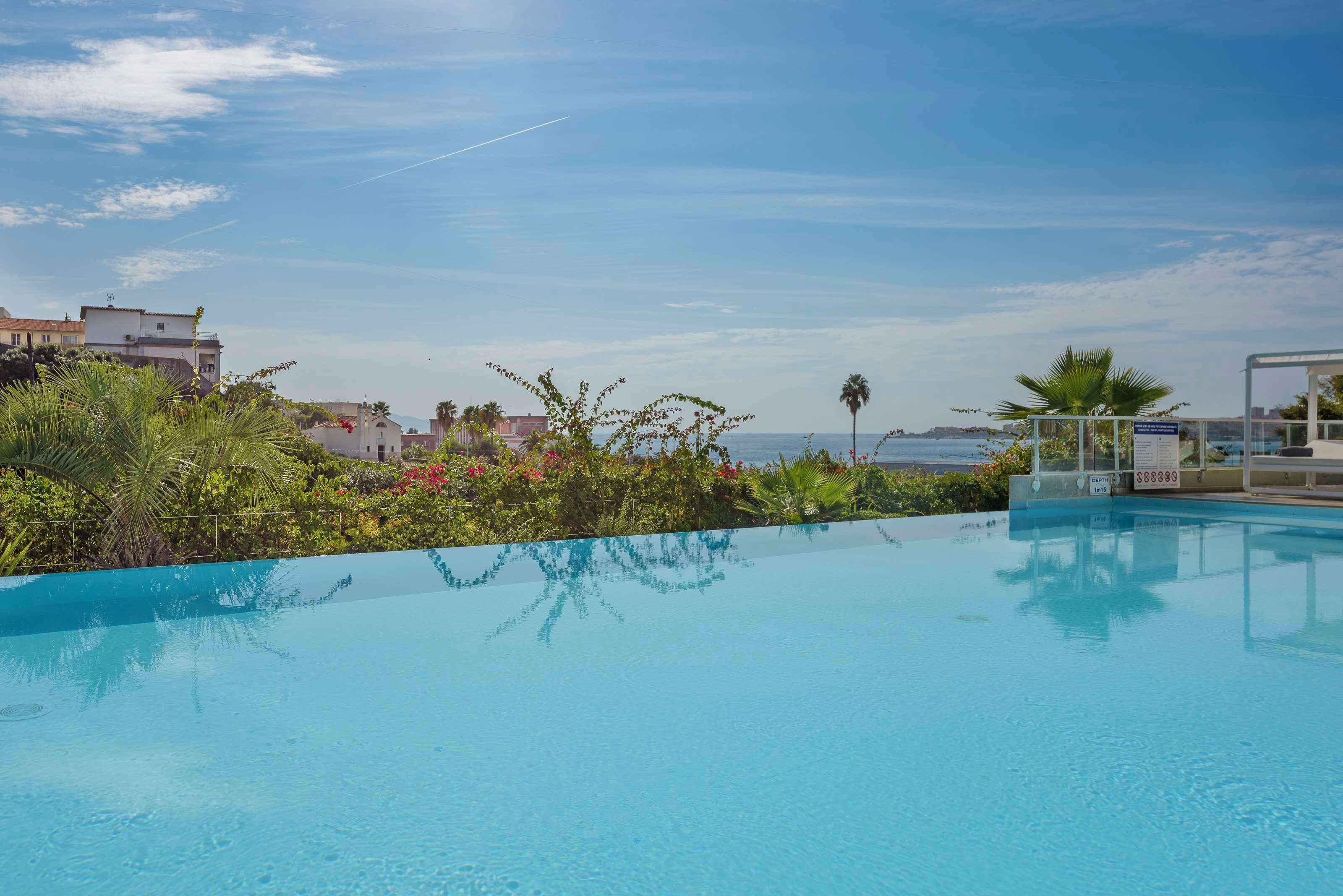 Ein klares, blaues Schwimmbecken mit Blick auf das Meer und Gebäude im Hintergrund.
