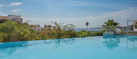 Ein klares, blaues Schwimmbecken mit Blick auf das Meer und Gebäude im Hintergrund.