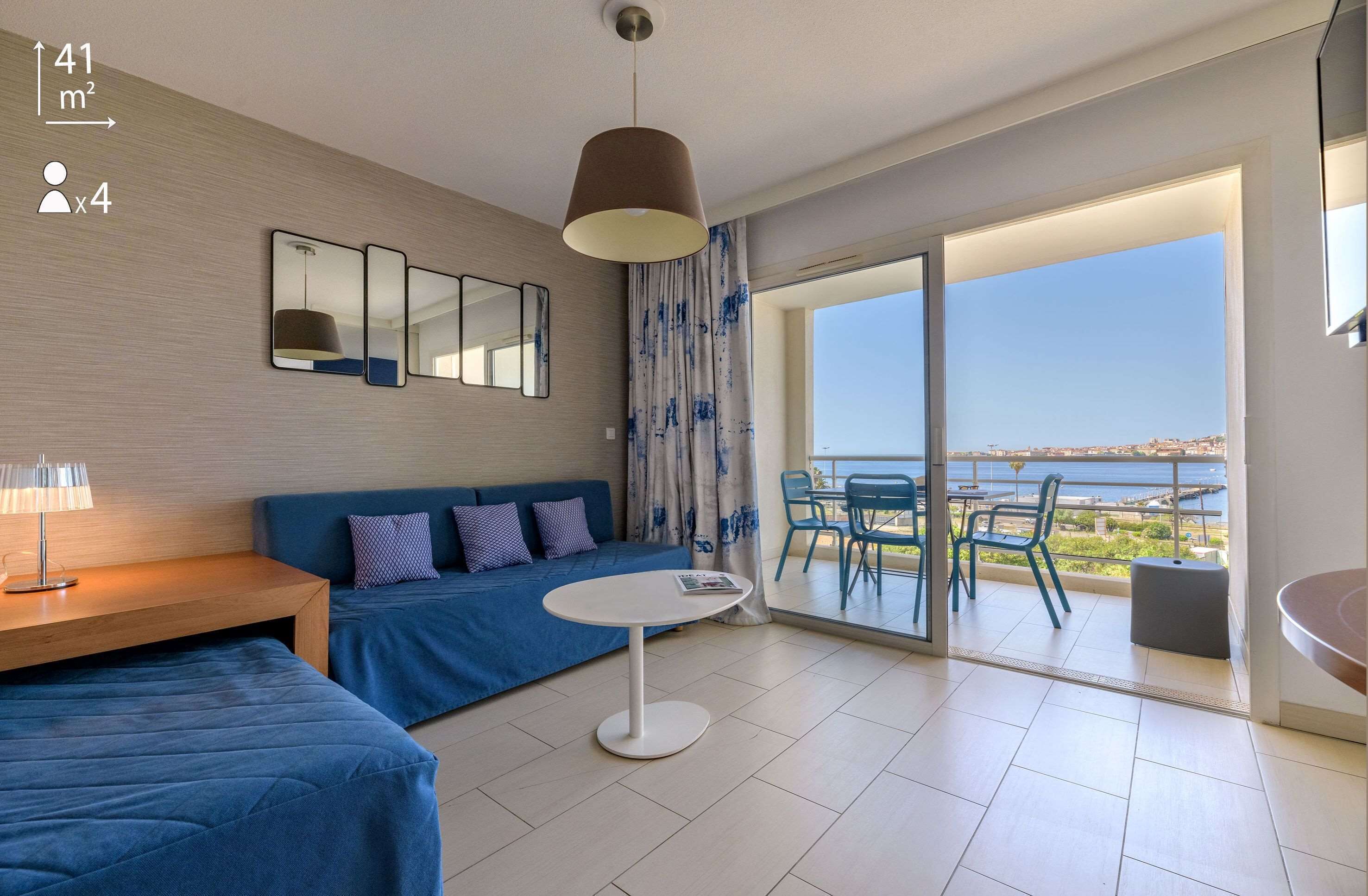 Habitació d'hotel moderna amb un balcó gran, un sofà, una taula petita i una làmpada penjant.