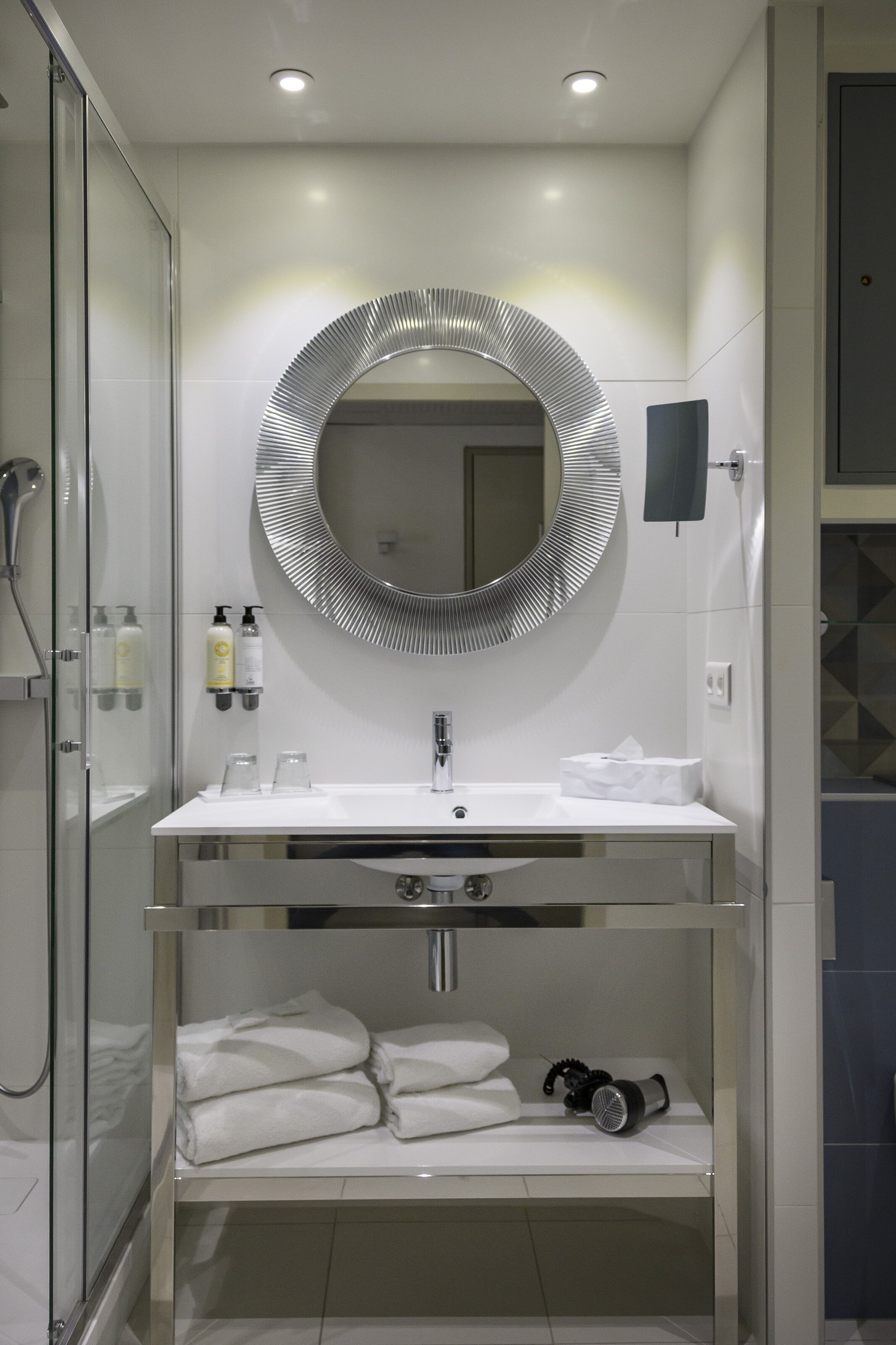 A modern bathroom with a glass-enclosed shower, a round mirror, a white sink, and a towel rack.