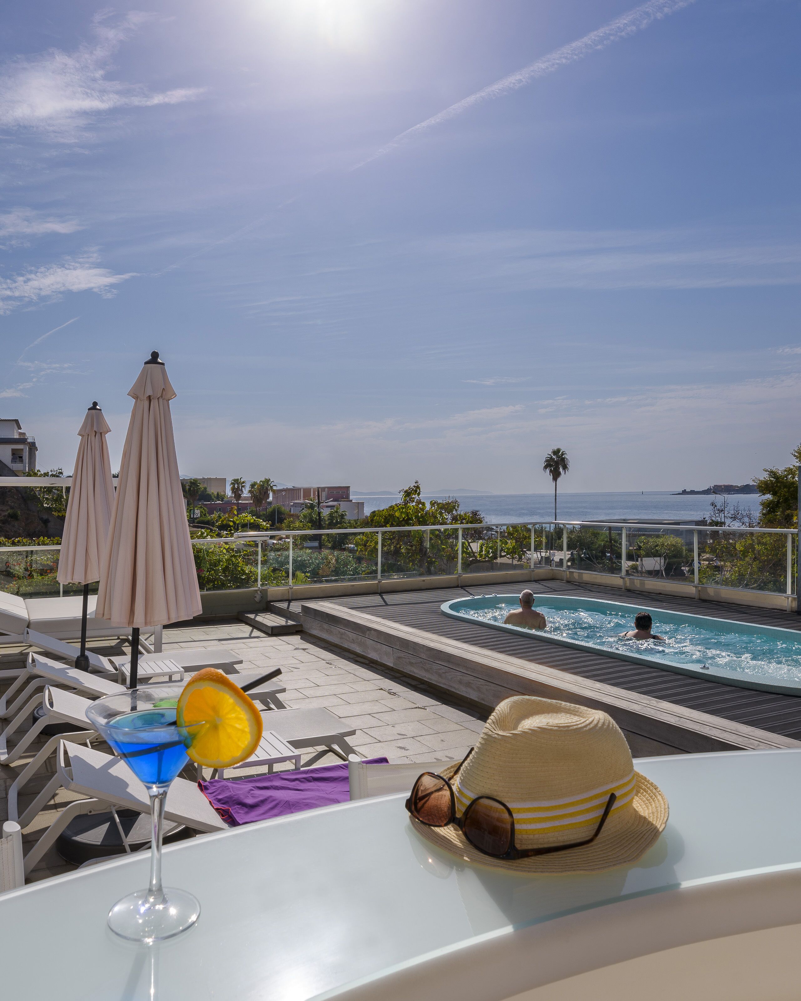 Ein Poolbereich auf dem Dach mit Liegestühlen, Sonnenschirmen und Blick auf das Meer.