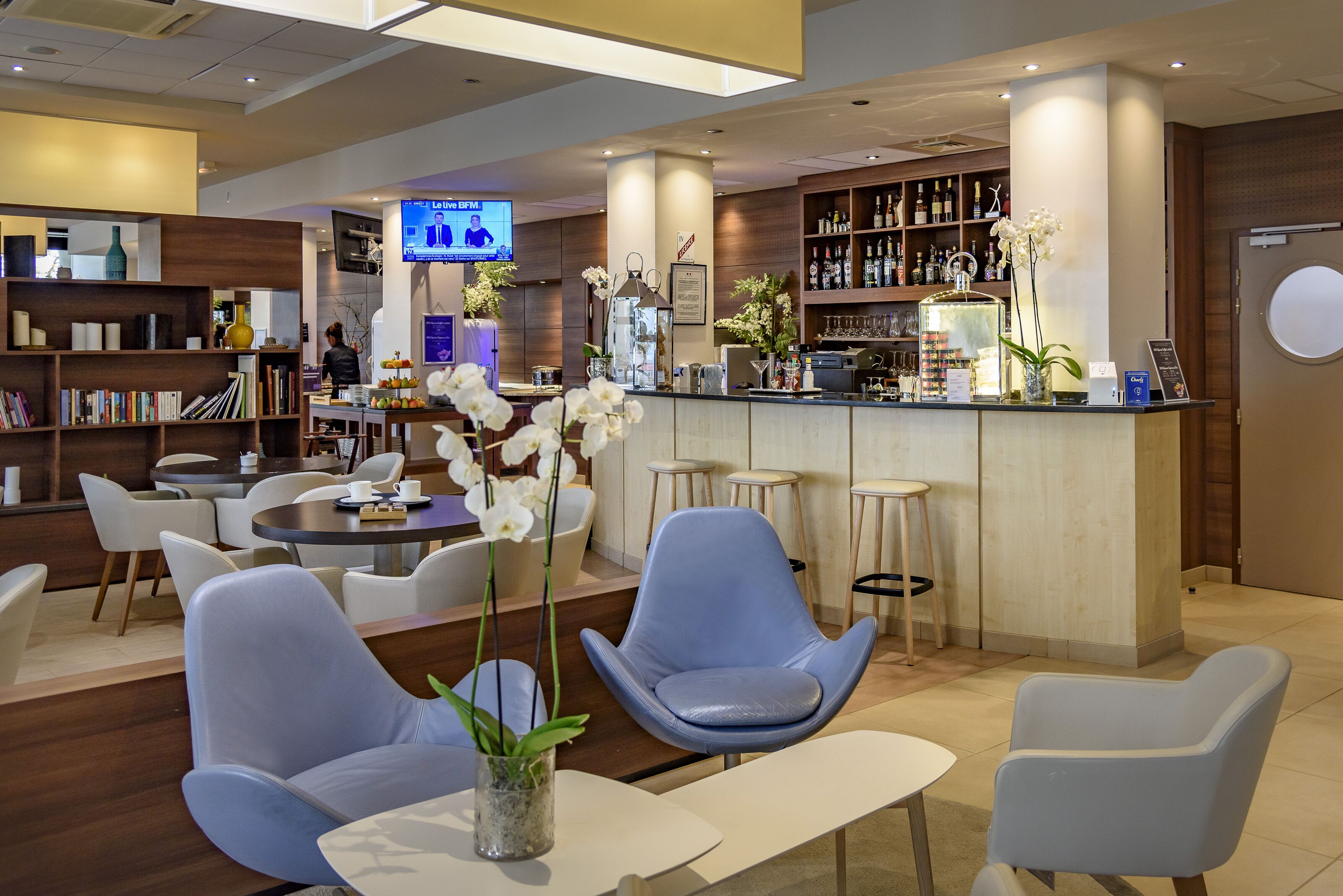 A modern hotel lobby with a bar area, seating arrangements, and a television screen.