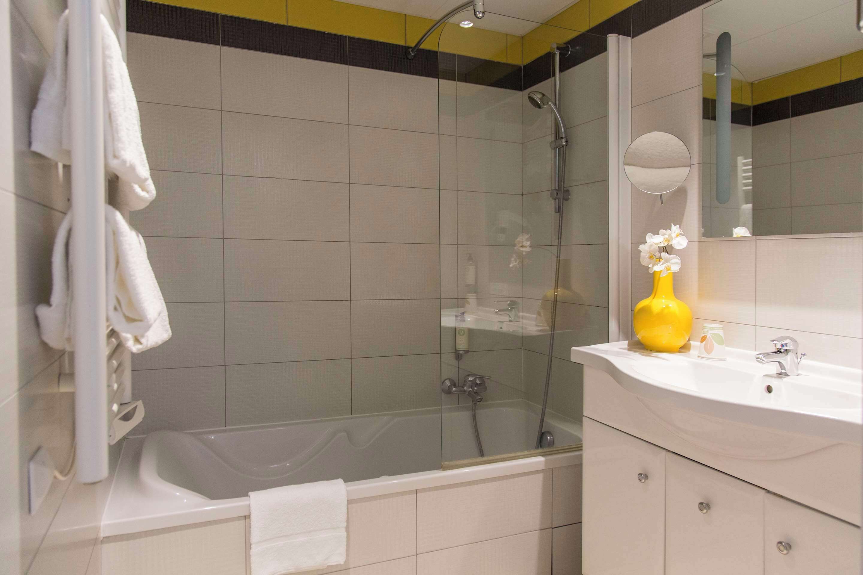 Ein modernes Badezimmer mit einer gläsernen Duschkabine, einer weißen Badewanne und einem Waschtisch mit Spiegel und gelber Vase.