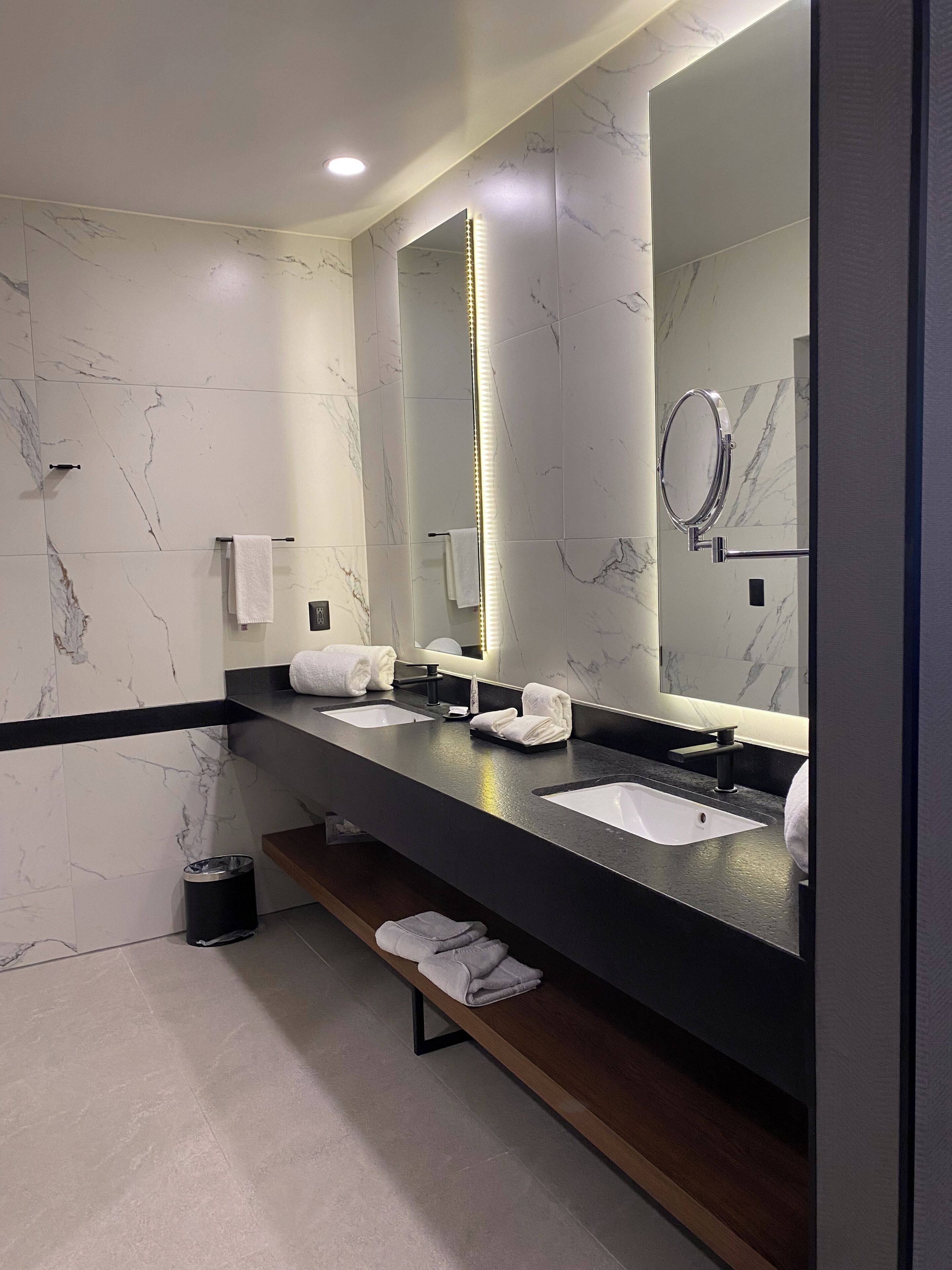 Un baño moderno con dos lavamanos, un espejo grande y un banco con toallas.