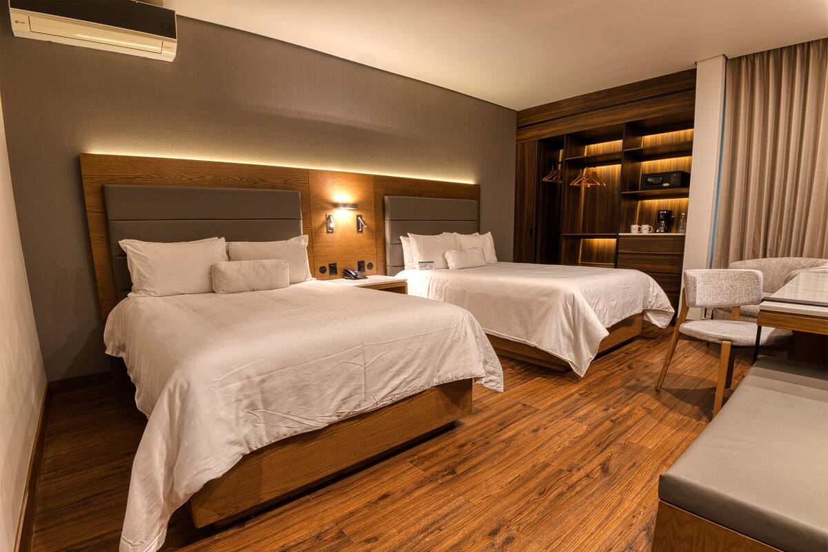 Une chambre d’hôtel avec deux lits, un plancher en bois, une armoire intégrée et un coin salon.
