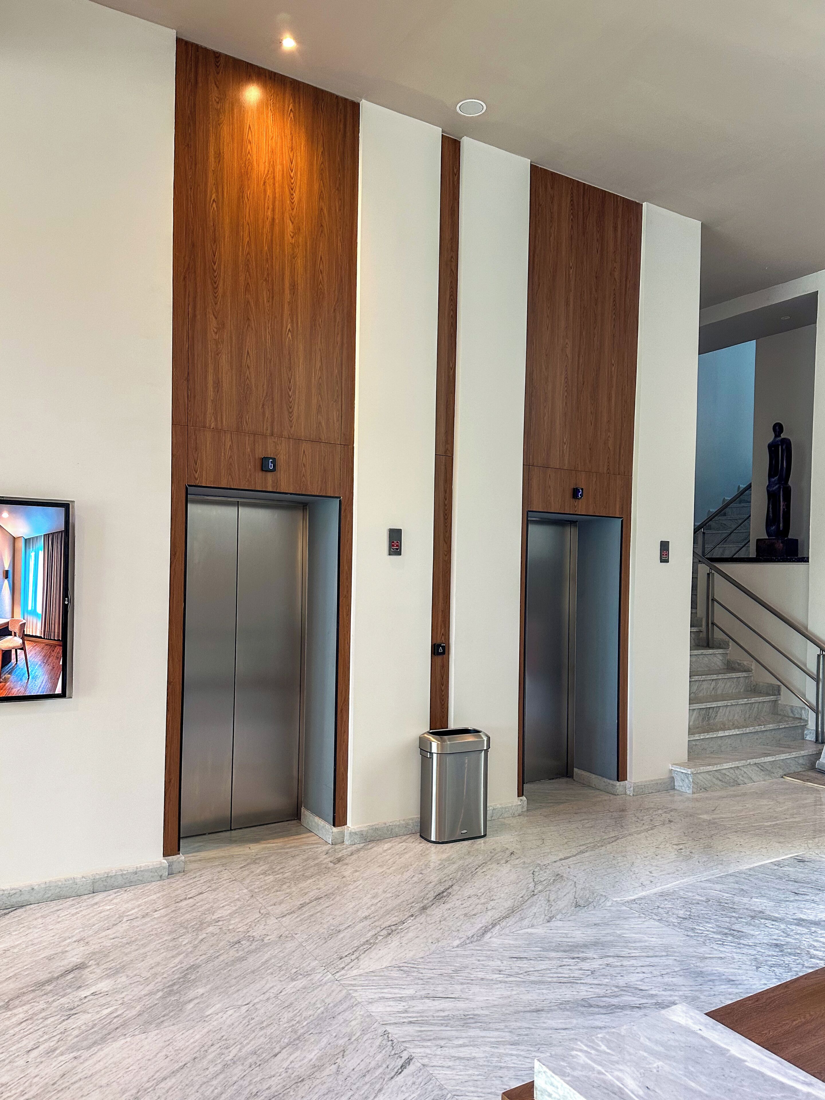 Eine moderne Lobby mit zwei Aufzügen, einem Marmorboden und einer Treppe.