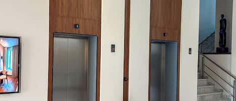 Eine moderne Lobby mit zwei Aufzügen, einem Marmorboden und einer Treppe.