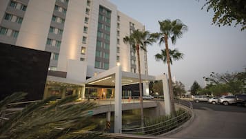 Un hotel moderno con entrada cubierta, palmeras y zona de estacionamiento.