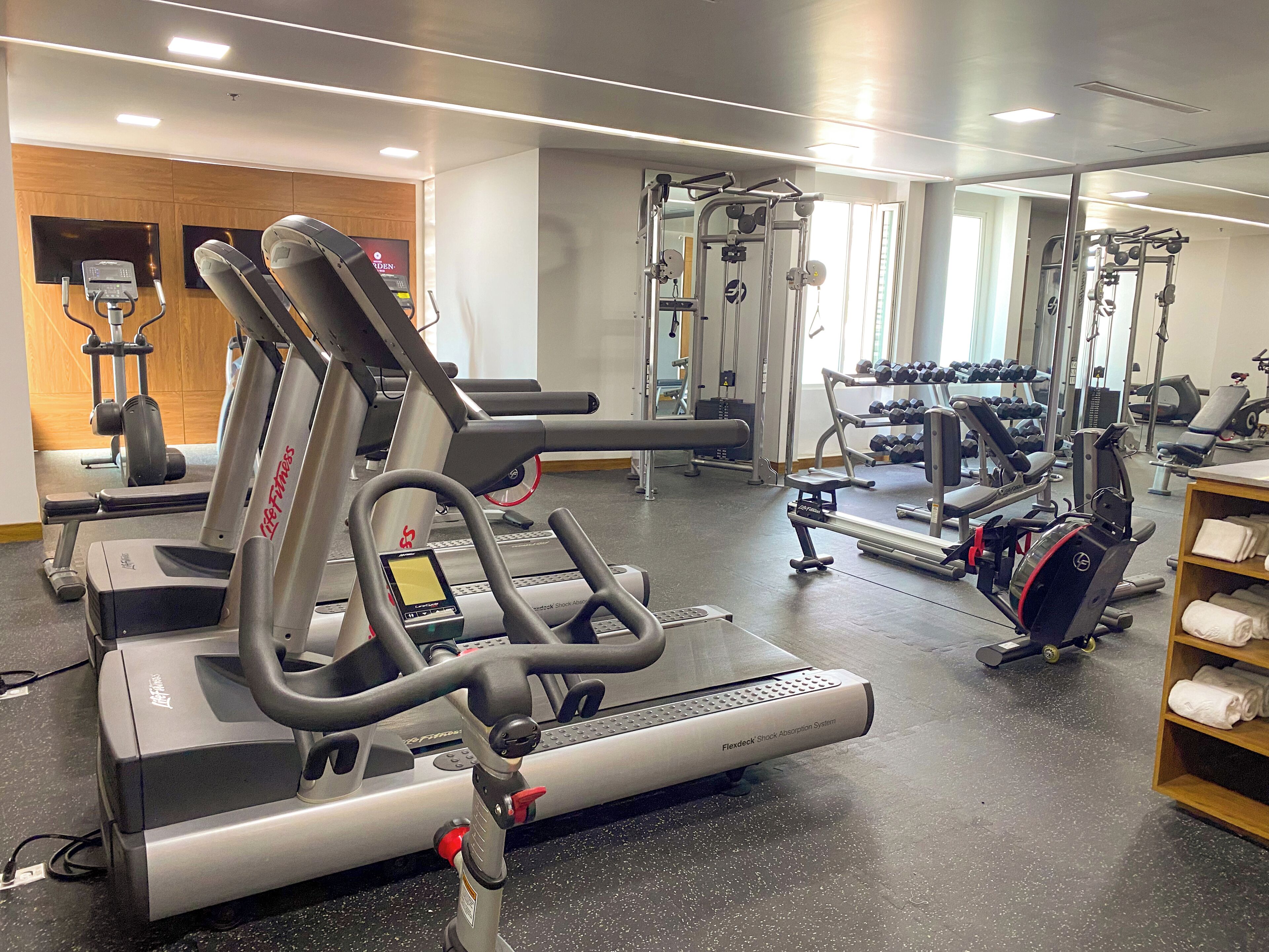 Un gimnasio con máquinas de cardio, equipo de levantamiento de pesas y un espejo grande.