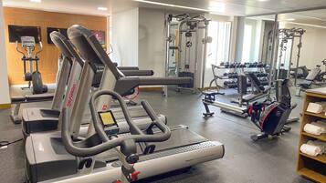 Un gimnasio con máquinas de cardio, equipo de levantamiento de pesas y un espejo grande.