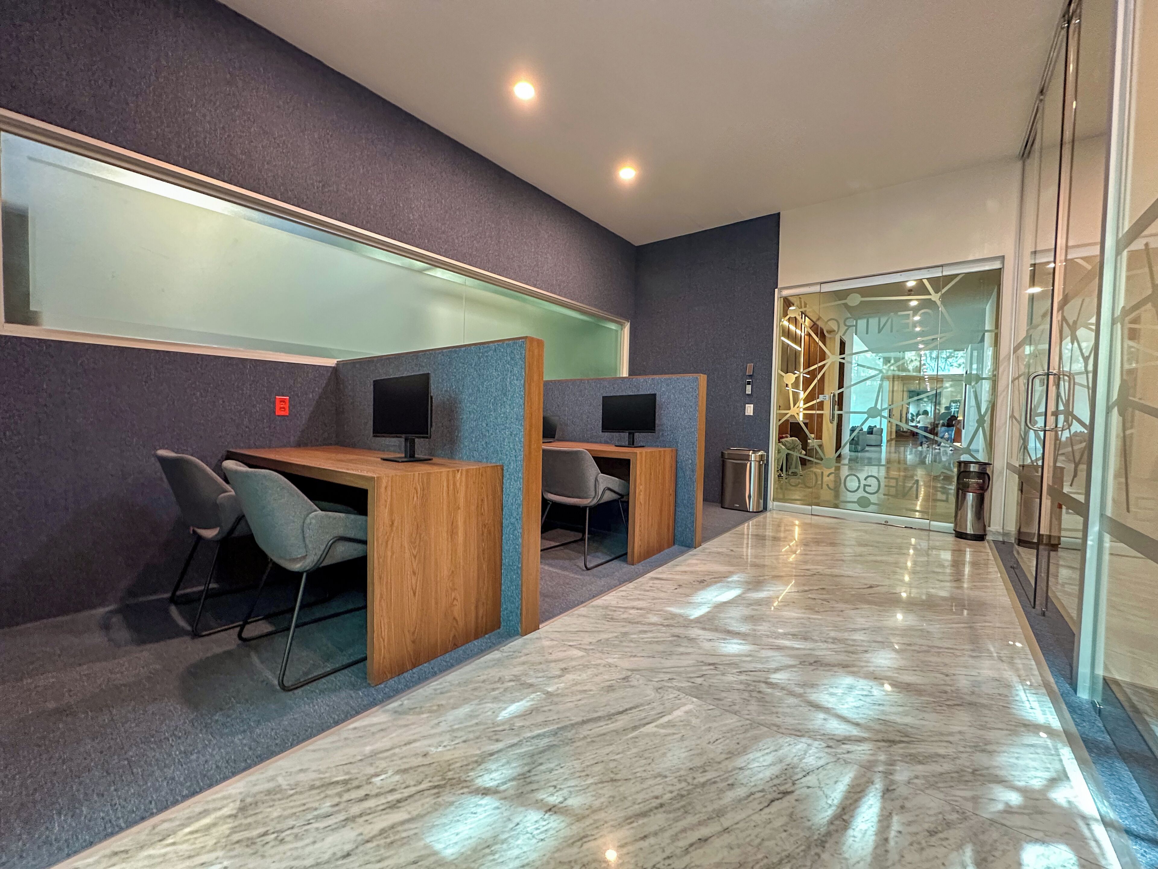 Un espacio de oficina moderno con cubículos, escritorios, sillas y un muro de vidrio.