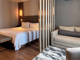 Una habitación de hotel moderna con cama, sofá, banqueta y alfombra estampada.