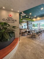Ein Restaurantinnenraum mit einem Schild, auf dem 'BISTRO GARDEN GRILL BAR' steht, Tischen, Stühlen und Zimmerpflanzen.