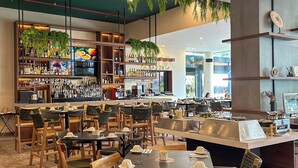 Ein Restaurant mit mehreren Tischen und Stühlen, einer Bar mit Regalen voller Flaschen und hängenden Pflanzen.
