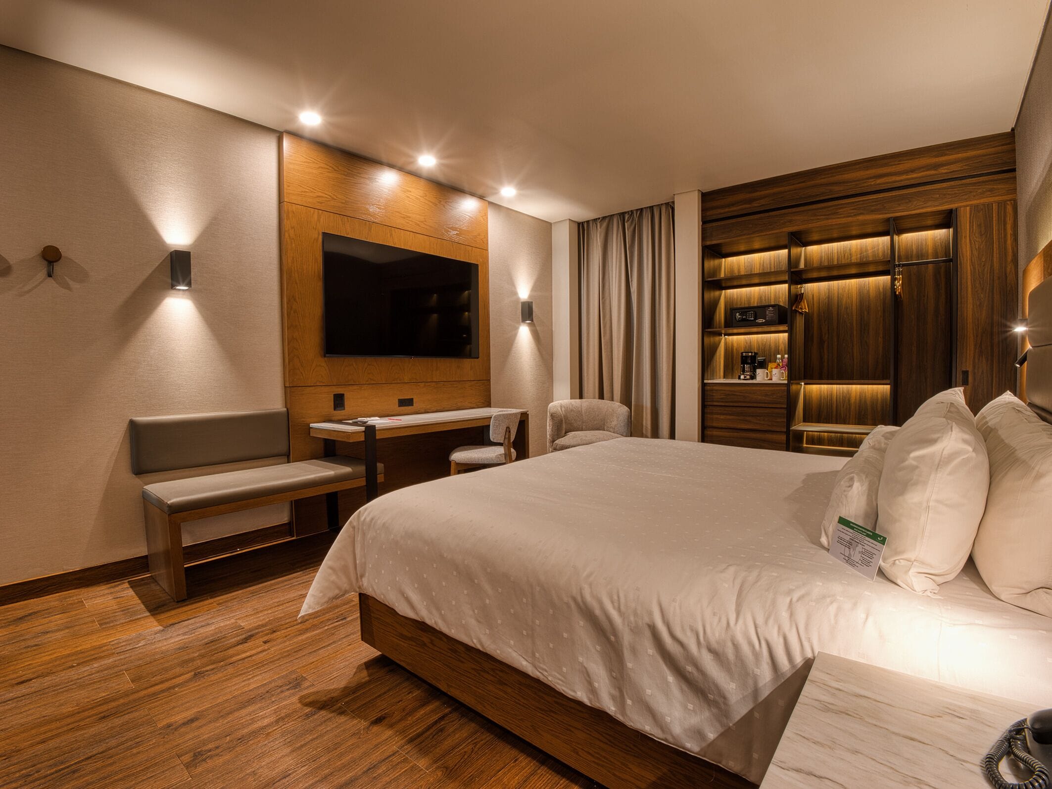 A hotel room with a large bed, a desk, a chair, a television, and a built-in wardrobe.
