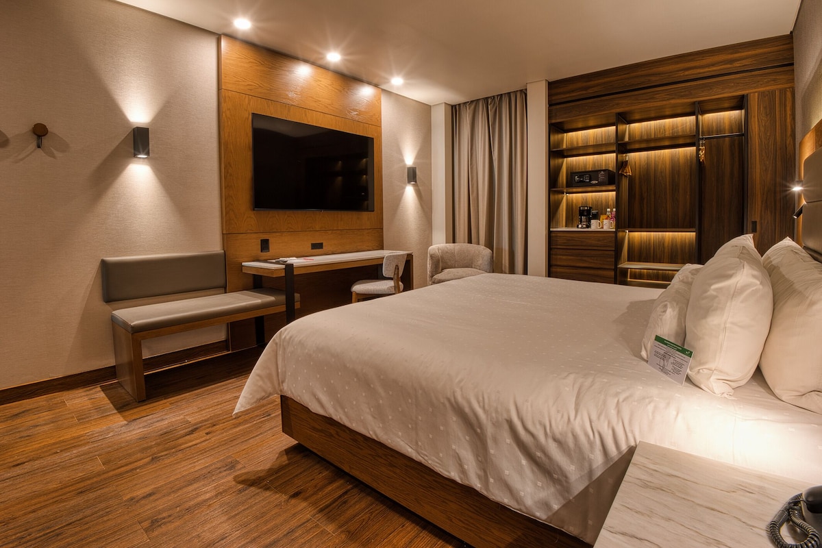Una habitación de hotel moderna con una cama grande, un escritorio, una silla, un televisor y un minibar.