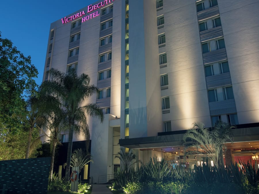 Een hotel met een zwembad aan de voorzijde, een bord met de tekst 'Victoria Ejecutivo Hotel' en een moderne gevel.
