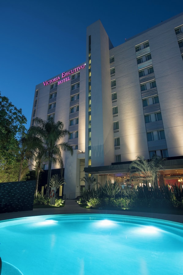 Un hotel con piscina al frente y un cartel que dice 'Victoria Ejecutivo Hotel', y una moderna fachada de edificio.