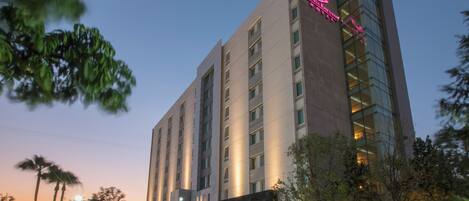 A multi-story hotel with a prominent sign, a parking lot, and a well-lit entrance.