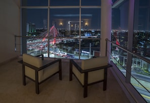 Habitación en un rascacielos con un amplio ventanal que da a un paisaje urbano nocturno, con un puente destacado y calles iluminadas.