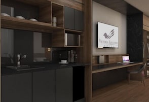 Cocina moderna con armarios oscuros, microondas integrado y cafetera. Hay un ordenador portátil sobre la encimera y una silla.
