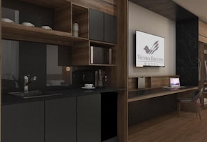 Cocina moderna con armarios oscuros, microondas integrado y cafetera. Hay un ordenador portátil sobre la encimera y una silla.