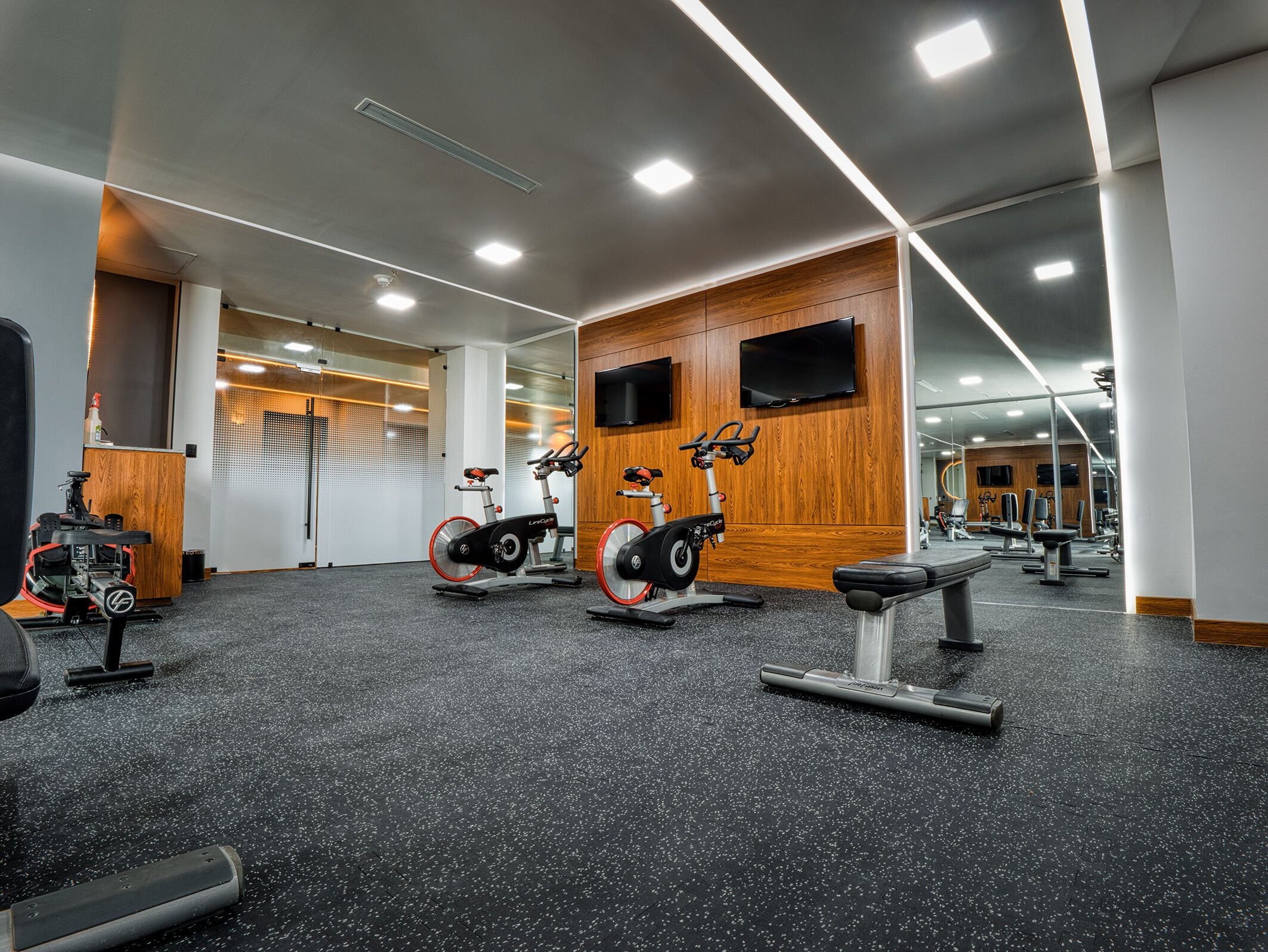 A gym with stationary bikes, a bench, and a mirror wall.