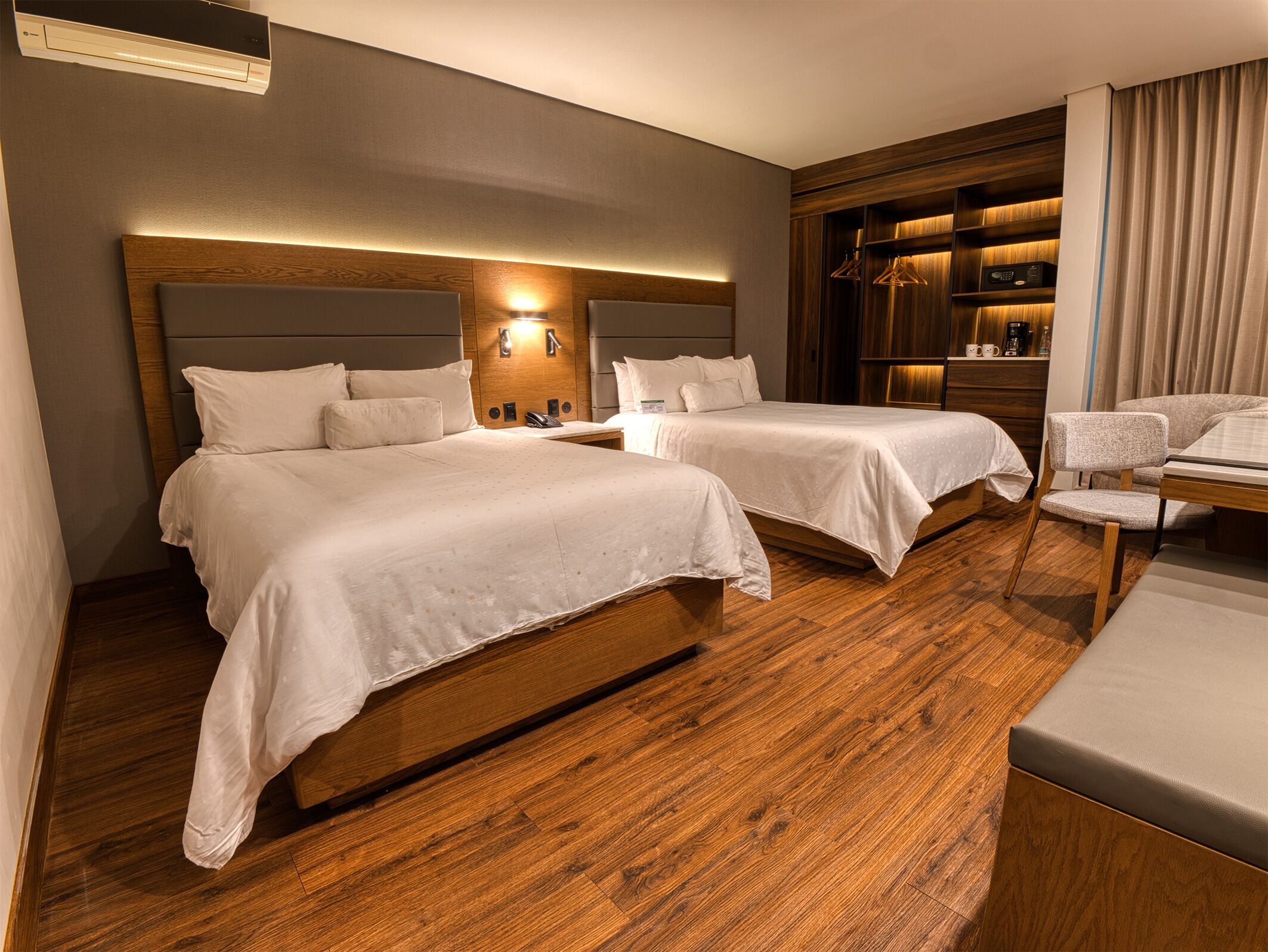 Une chambre d’hôtel avec deux lits, un bureau, une chaise et un mini-bar intégré.