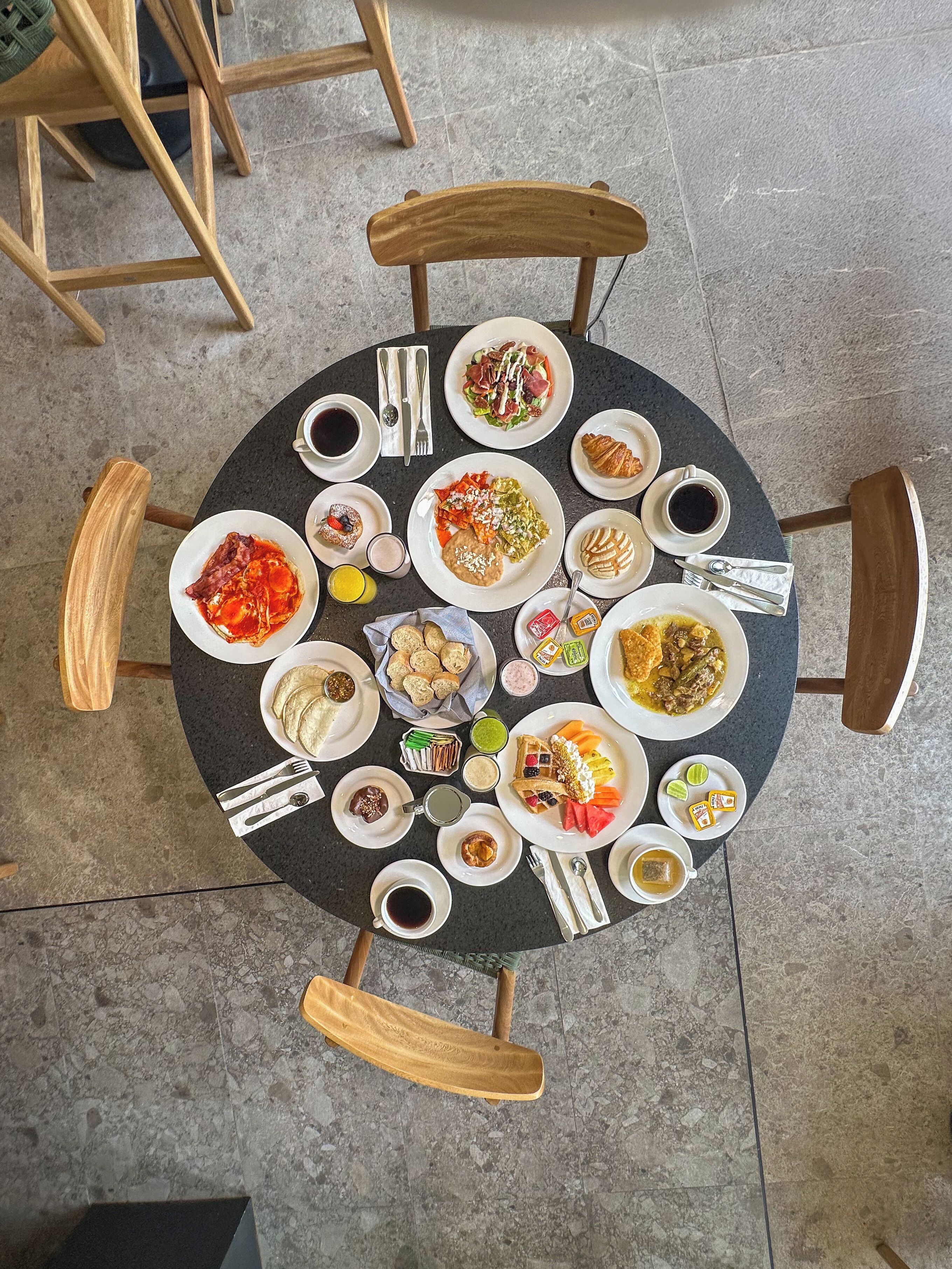 A round table with various dishes and drinks, surrounded by wooden chairs.