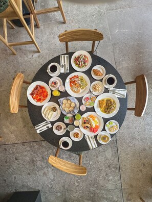 Una mesa redonda con diversos platos y bebidas, rodeada de sillas de madera.