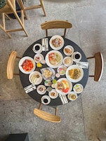 Uma mesa redonda com vários pratos e bebidas, rodeada por cadeiras de madeira.
