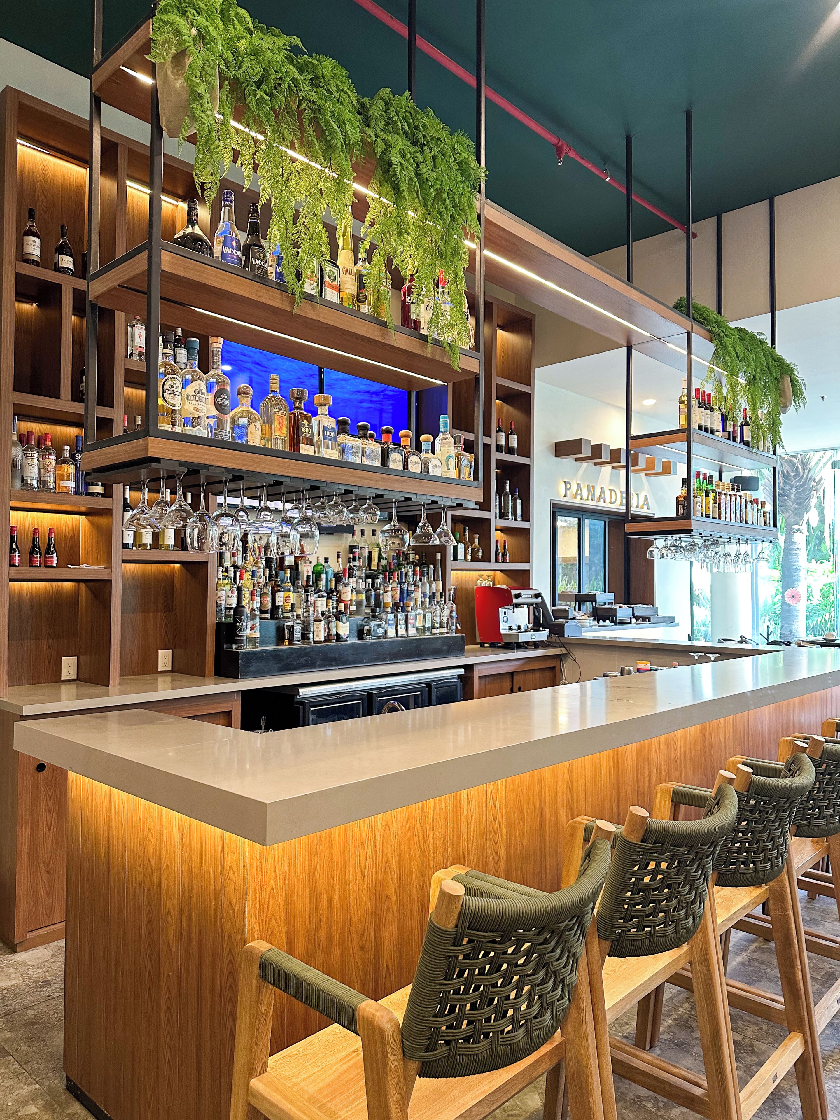 A bar area with shelves of liquor bottles, a coffee machine, and wicker chairs.