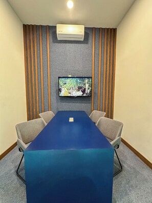 Un salón de conferencias con una mesa azul, cuatro sillas, un televisor de pantalla plana montado y un equipo de aire acondicionado.