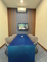 Un salón de conferencias con una mesa azul, cuatro sillas, un televisor de pantalla plana montado y un equipo de aire acondicionado.