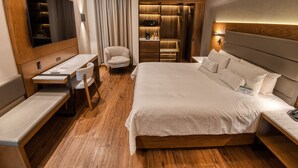Une chambre d’hôtel avec un plancher en bois, un lit avec du linge de maison blanc, un bureau avec une chaise, une télévision et un minibar.