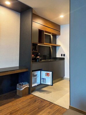 Una cocina compacta con microondas integrado, un refrigerador pequeño y un basurero.
