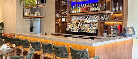 A bar area with multiple shelves of liquor bottles and glasses, wooden chairs, and a counter with a coffee machine.