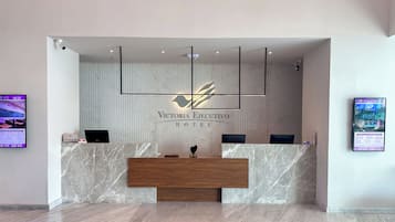 Un mostrador de recepción de hotel con encimera de mármol, dos monitores y una lámpara moderna.