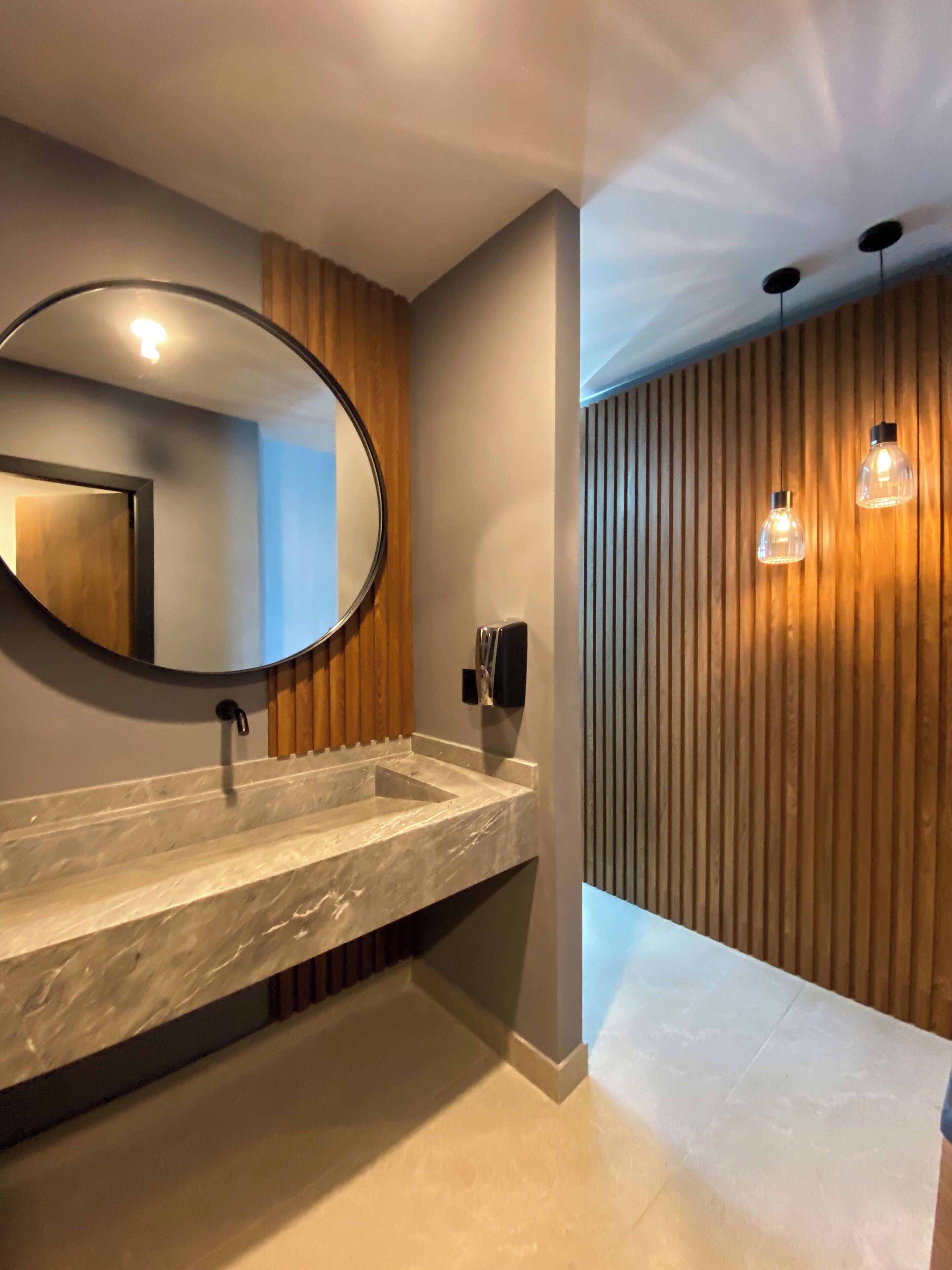A modern bathroom with a marble sink, a large mirror, and wooden paneling on the wall.