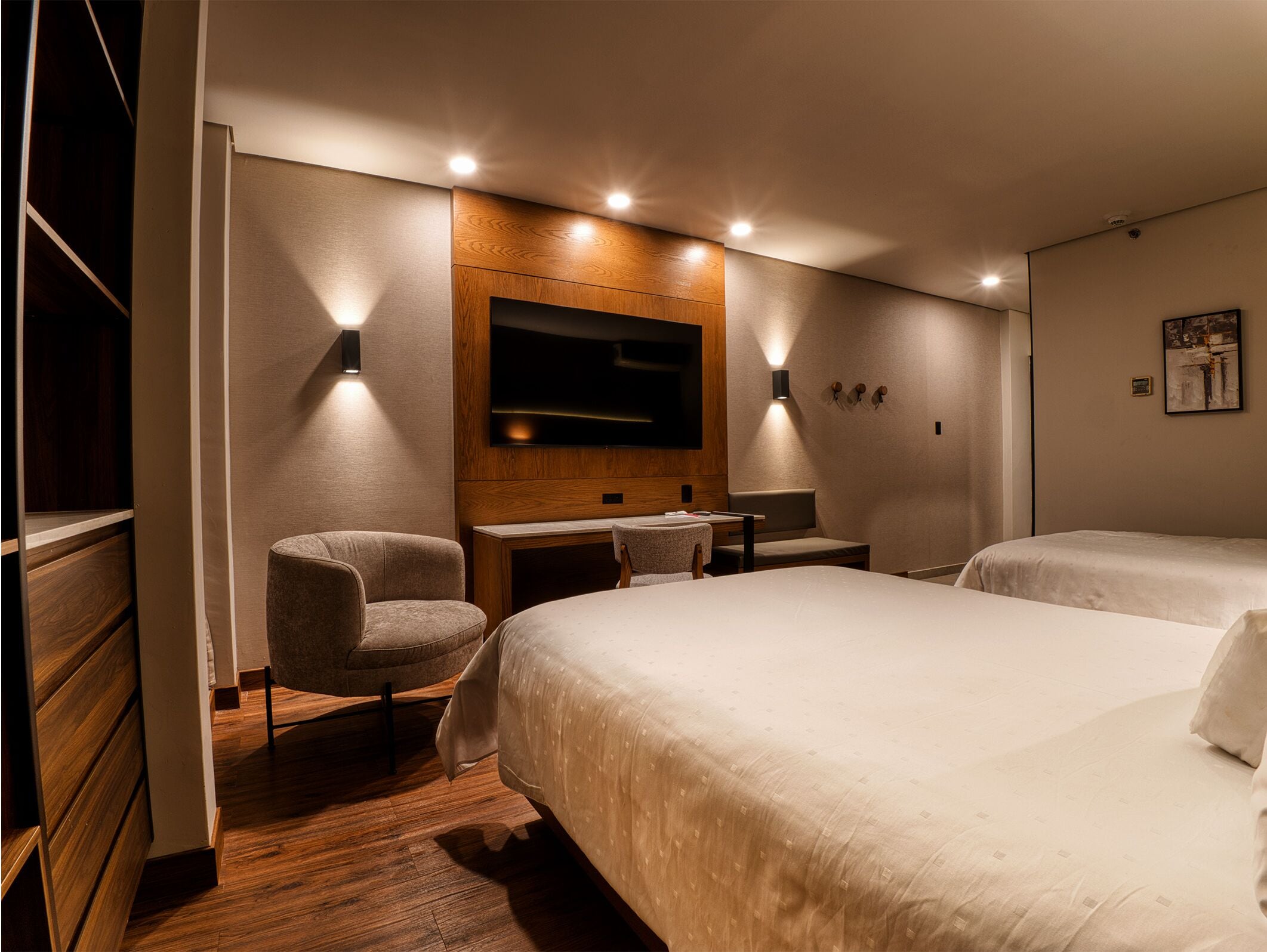 Habitación de hotel con una cama grande, un escritorio, una silla, un televisor montado en la pared y suelo de madera.