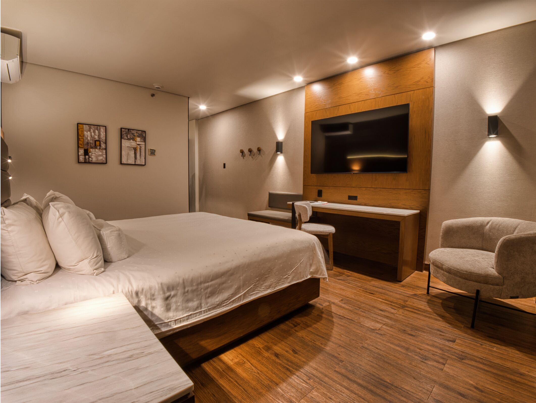 A modern hotel room with a large bed, a desk, a chair, and a flat-screen TV mounted on the wall.