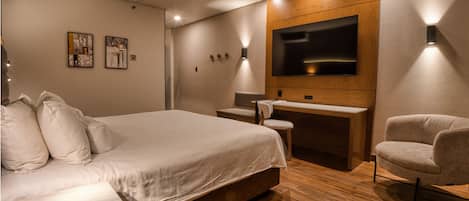 A modern hotel room with a large bed, a desk, a chair, and a flat-screen TV mounted on the wall.