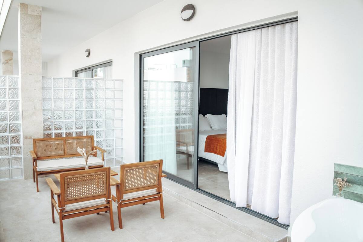 A balcony with wicker furniture, a sliding glass door leading to a bedroom, and a tiled floor.