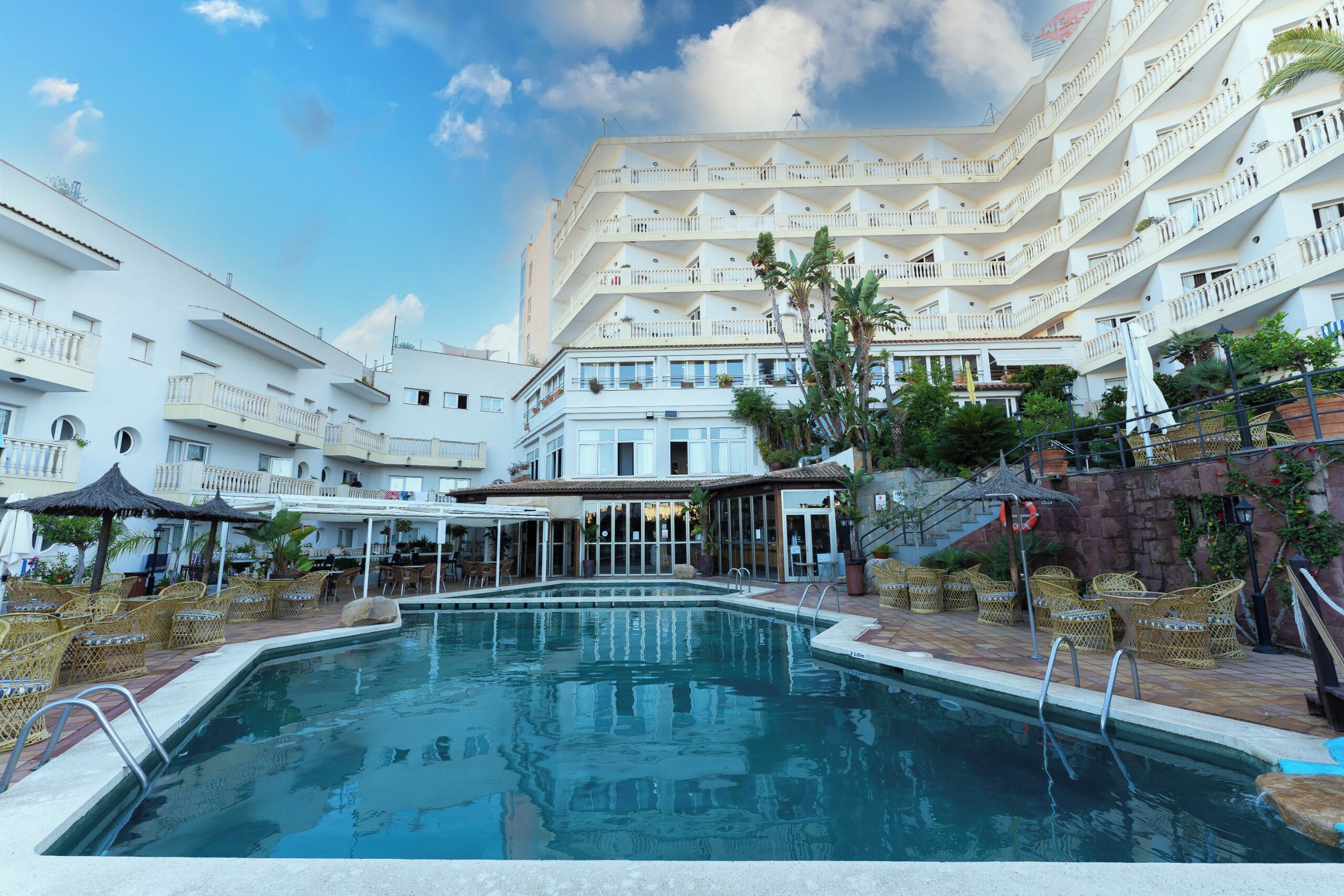Un hotel con piscina, mobiliario exterior y varios balcones.
